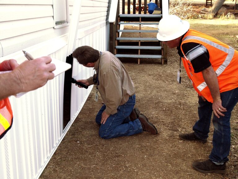 County building inspector examining the piers under a factory-built home while a contractor looks on