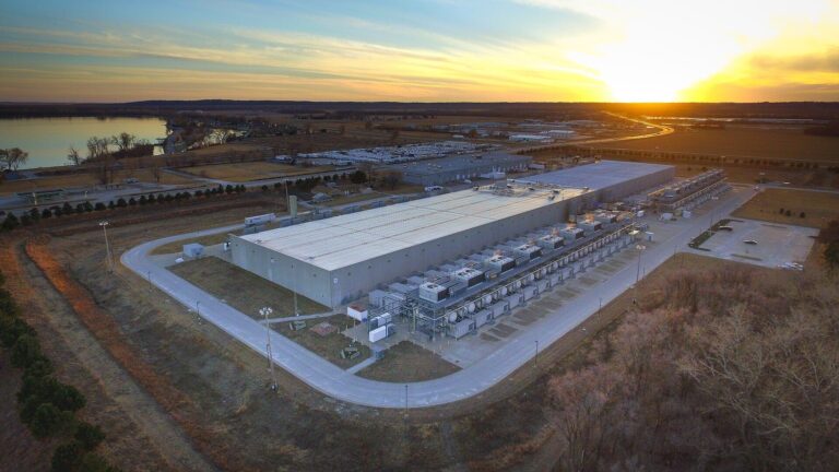 Aerial view of the Google data center in Council Bluffs, Iowa, a long gray building with rooftop cooling equipment beside a river at sunset