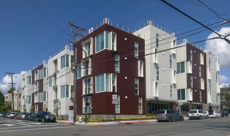 Finished four-story modular apartment building with red and white facades on a city street in Berkeley, California