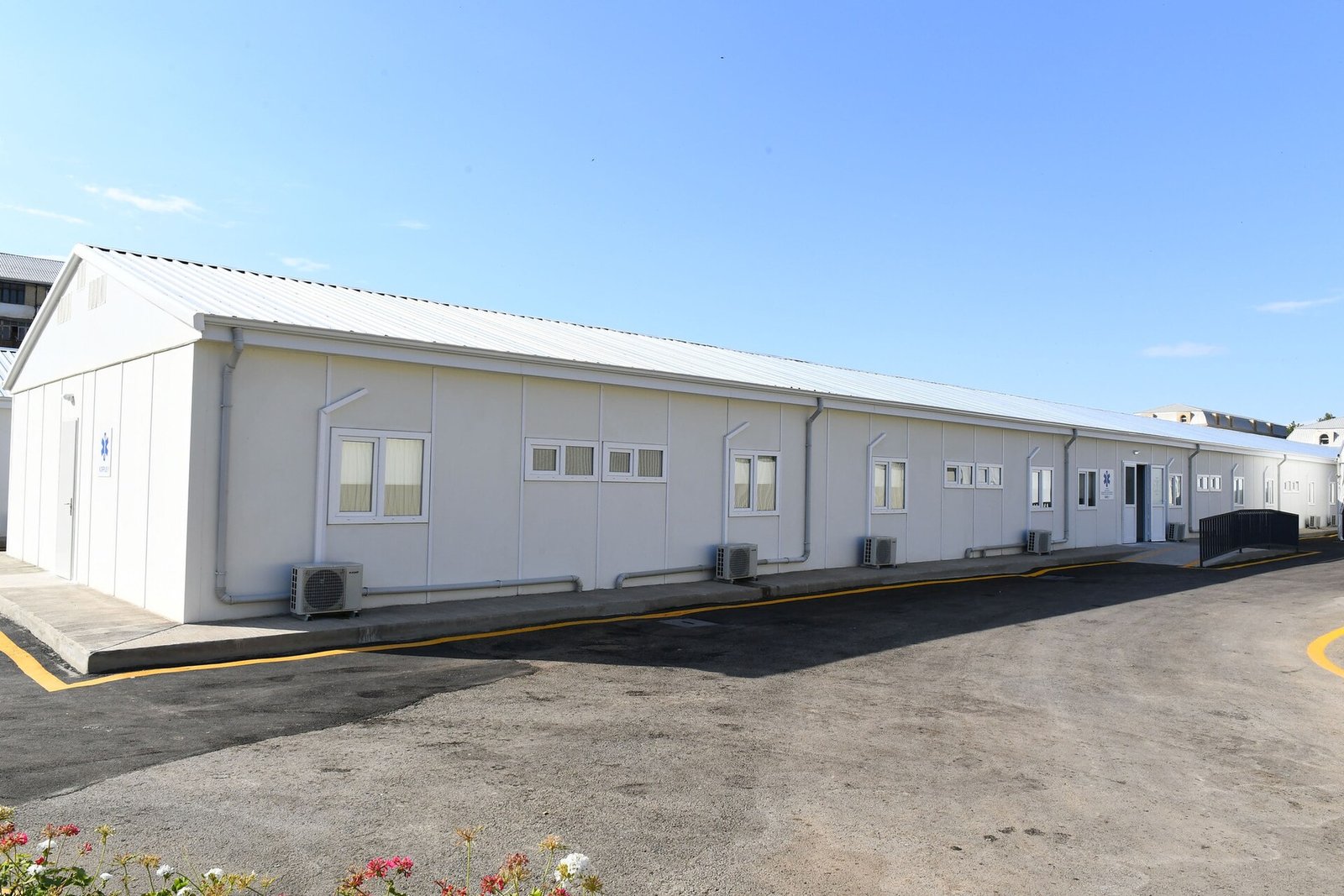 Single-story white modular hospital building with rows of windows under a blue sky