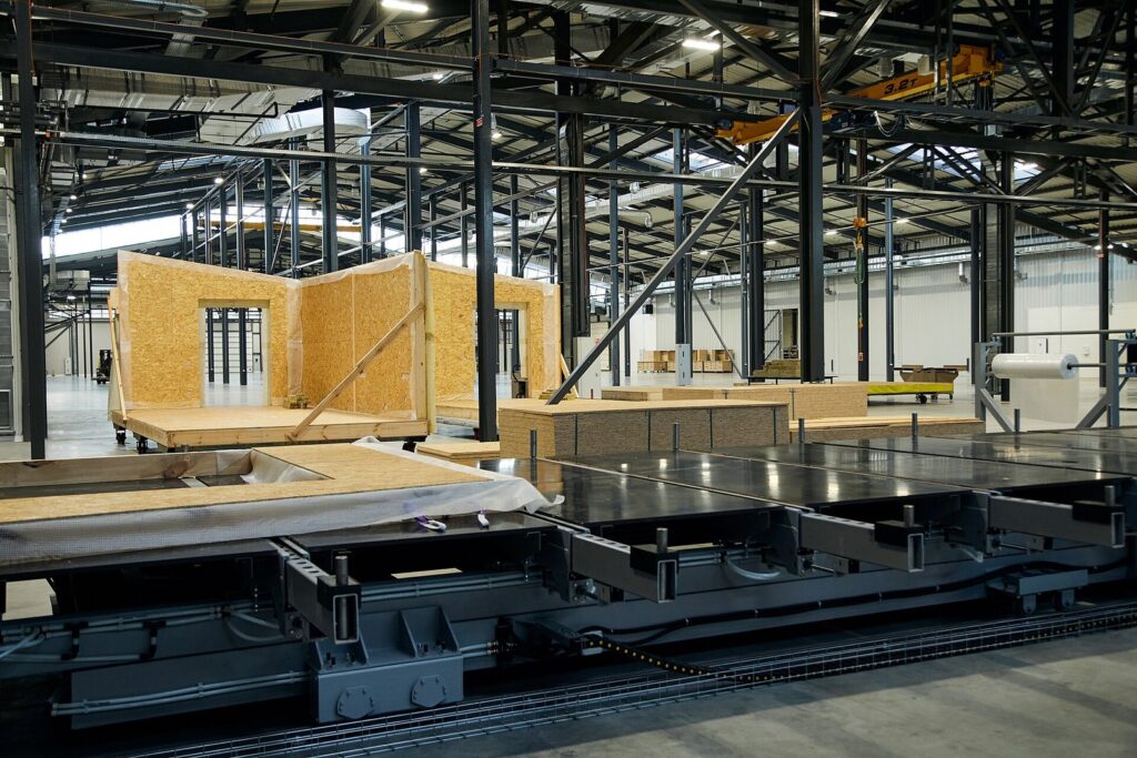Workers assembling timber house components on the production floor of a prefab home factory