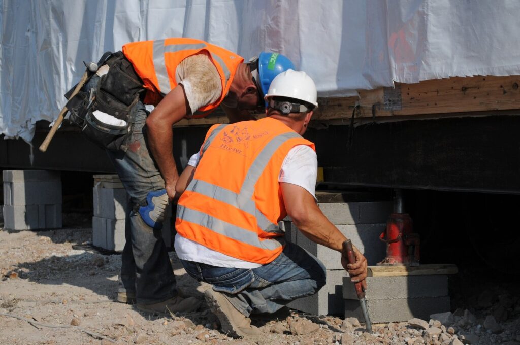 Construction worker setting concrete blocks to support a modular classroom building on its foundation