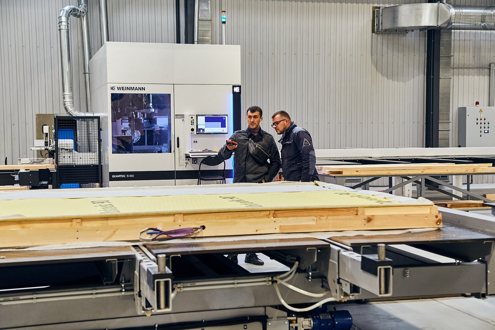 Workers operating an automated wall panel production line inside a prefab house factory
