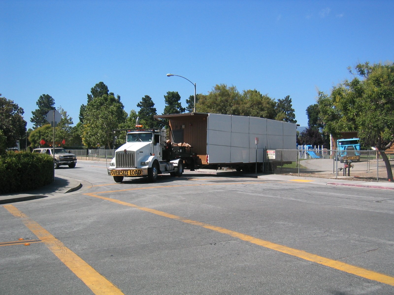 Half of a portable modular classroom loaded on a flatbed truck leaving a school site as a wide load