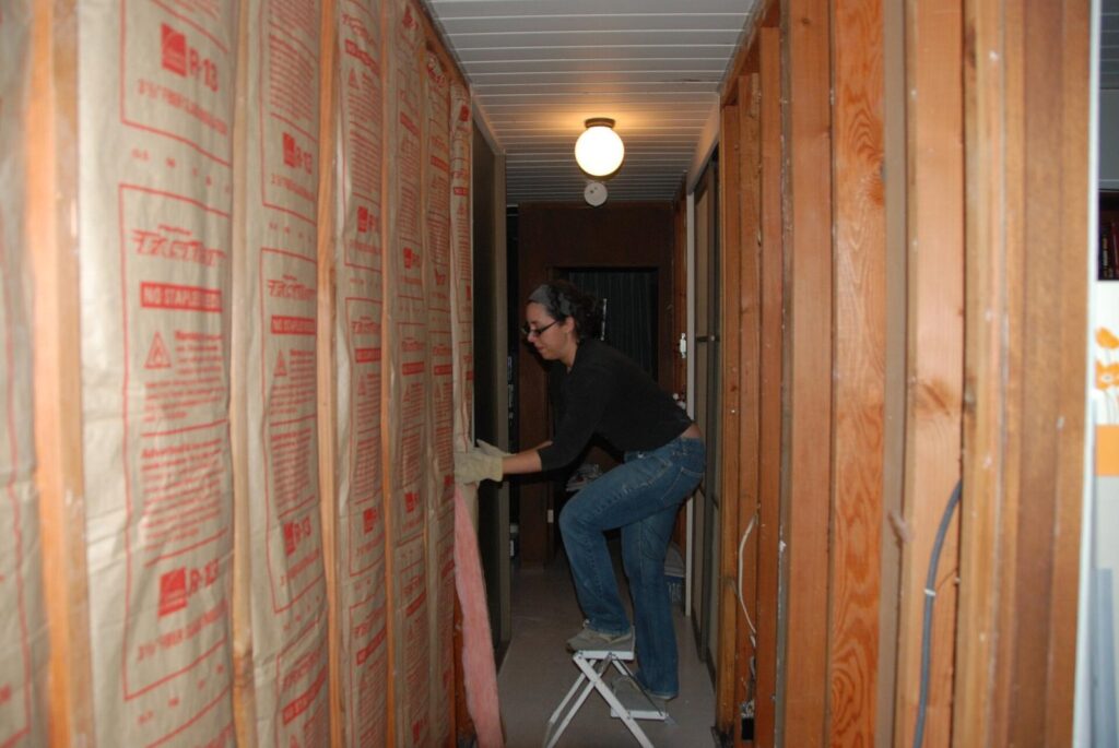 Worker installing insulation between wood studs in a narrow wall cavity during construction