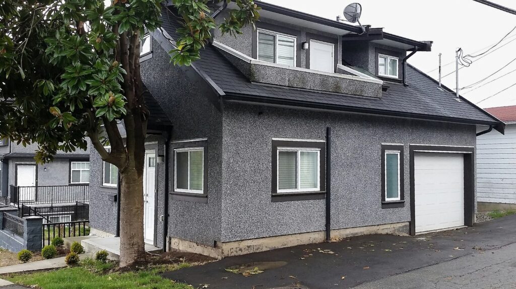 Gray two-story laneway house with a garage door facing a back lane in East Vancouver