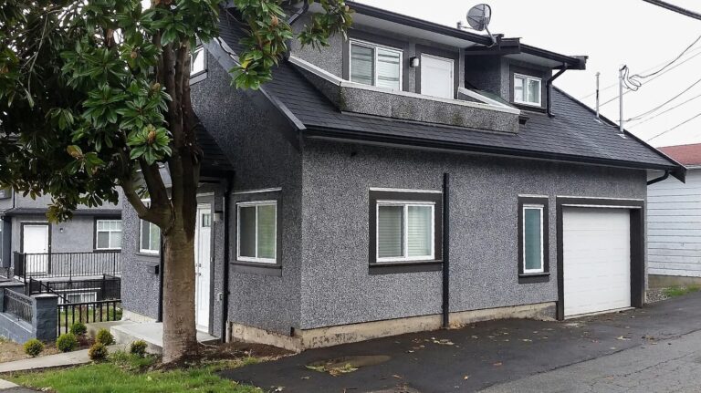 Gray two-story laneway house with a garage door facing a back lane in East Vancouver