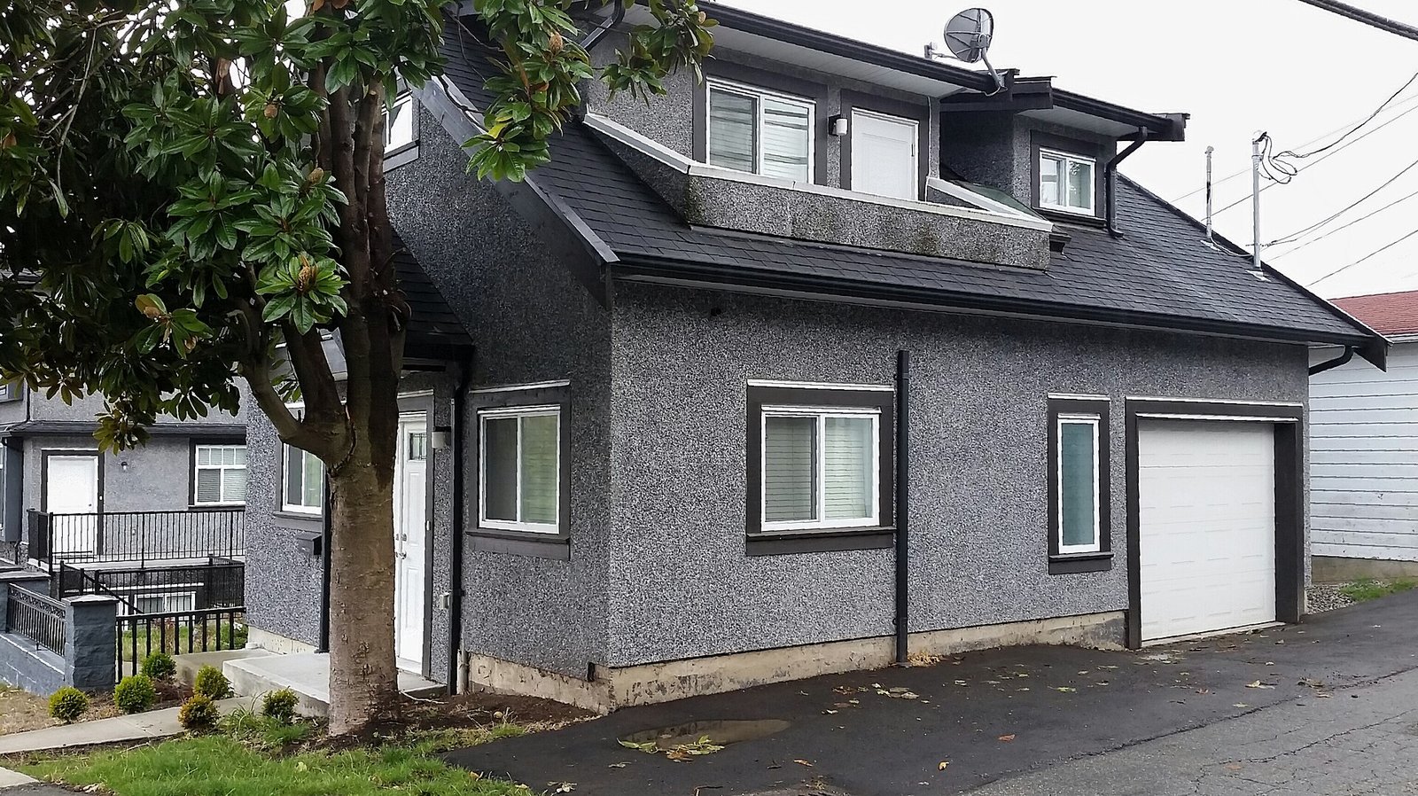 Gray two-story laneway house with a garage door facing a back lane in East Vancouver