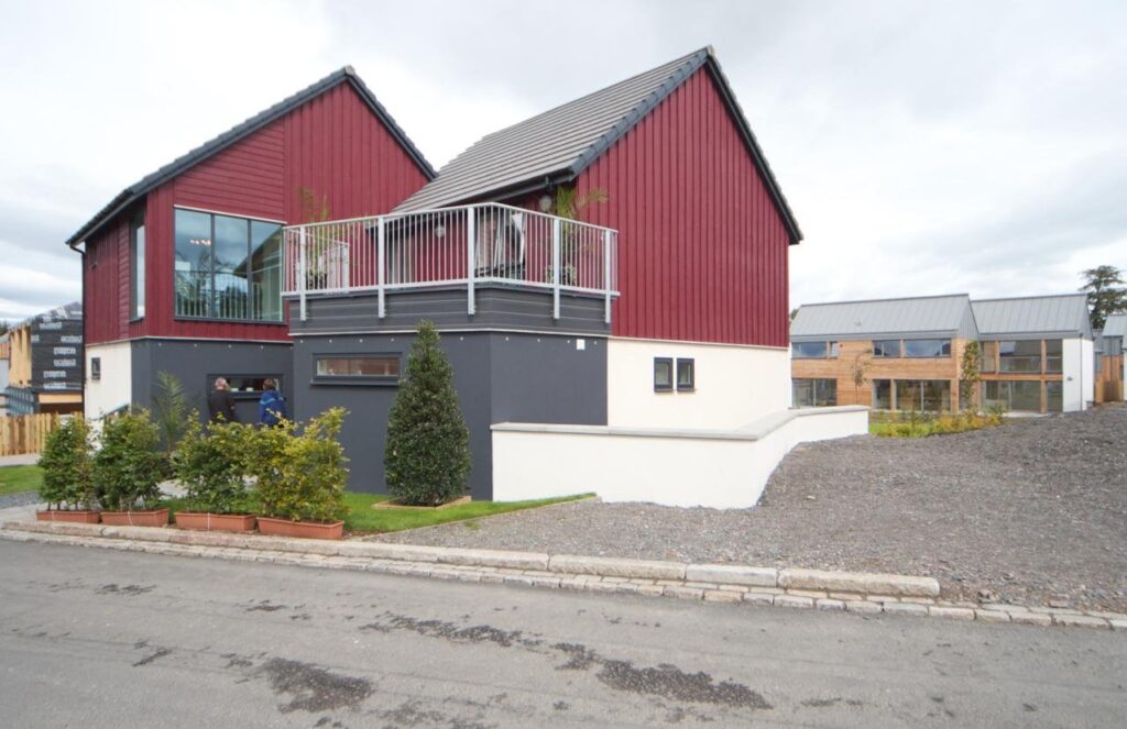 Finished two-storey modular house with red timber cladding and a balcony, beside other modular homes