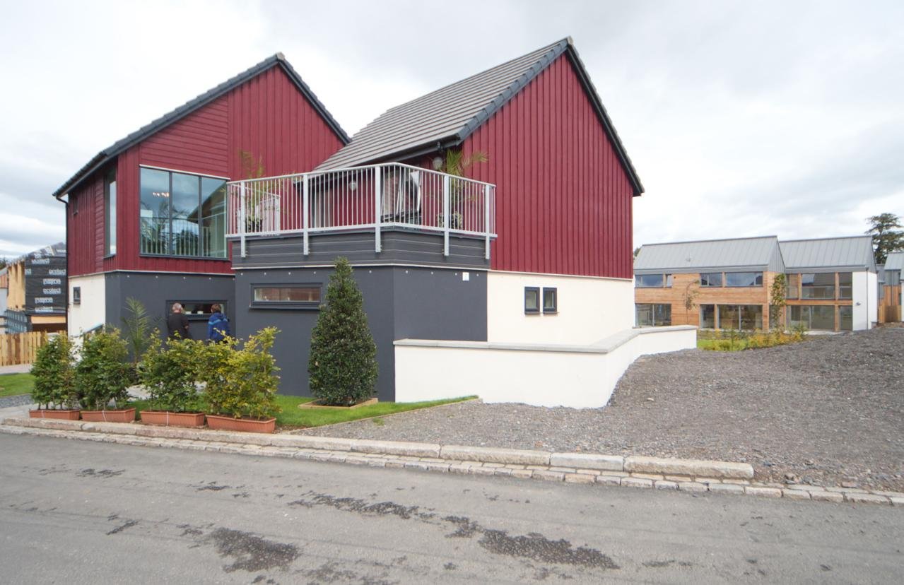 Finished two-storey modular house with red timber cladding and a balcony, beside other modular homes
